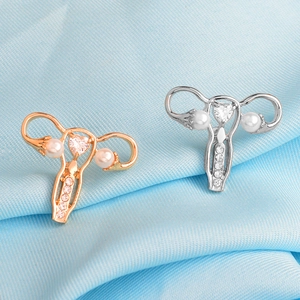 Macro shot of uterus-shaped badges with heart zircons and pearls on blue silk