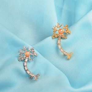 Detailed view of silver and gold neuron brooches with orange pearls on blue silk