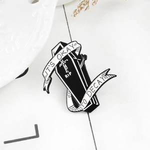 Punk style black coffin enamel pin with white ribbon and RIP text on a white desk