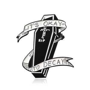 Gothic punk enamel pin featuring a black coffin with RIP cross and white ribbon design