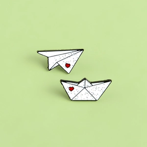 Minimalist enamel origami plane and boat brooches with red hearts on green background
