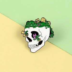 Detail shot of a skull enamel brooch with green succulents and a cat in the eye socket