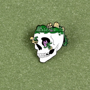 Detail of skull enamel pin with mushrooms, forest plants and purple cat creature