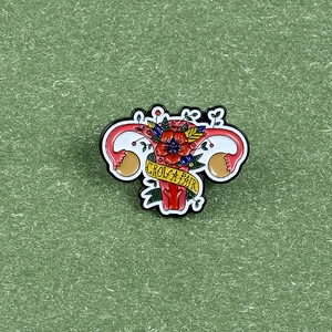 Enamel floral uterus pin with yellow ribbon and 'GROW A PAIR' text banner on green surface