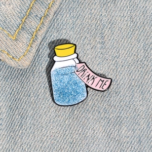 Detail view of a Drink Me potion bottle enamel pin pinned on a blue denim jacket texture