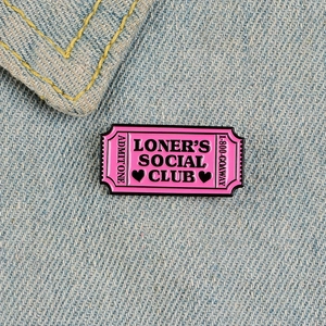 Pink ticket enamel pin with Loner's Social Club text on blue denim fabric background