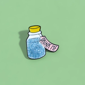 Creative Alice in Wonderland Drink Me enamel pin with blue glitter liquid on mint background