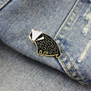 Détail d'une broche en émail représentant un blaireau sur tissu denim bleu avec dorure
