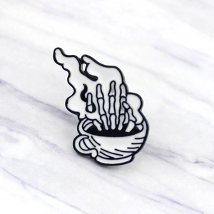 Detailed enamel pin showing a skeletal hand in a coffee cup with smoke detail