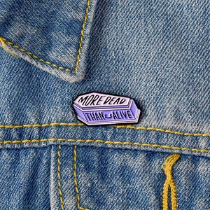 Gothic purple coffin enamel pin with MORE DEAD THAN ALIVE text on denim jacket