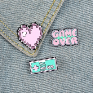 Three-piece retro game controller and pixel heart enamel pins on blue denim jacket