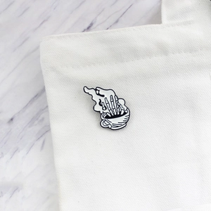Creative skeleton hand in coffee cup enamel pin on a white canvas bag accessory