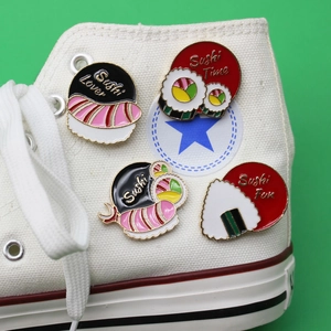 Set of four sushi enamel pins including salmon and rice ball designs on a white canvas shoe