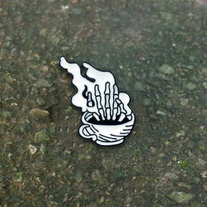 Creative punk enamel pin featuring skeleton hand in coffee cup on a stone texture background