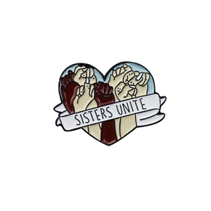 Broche cœur émaillée avec poings et texte Sisters Unite sur fond blanc neutre