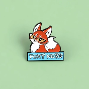 Cartoon orange fox enamel pin wearing glasses with Foxy Nerd text banner on green background