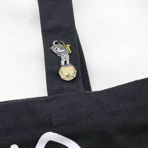 Creative enamel astronaut brooch playing saxophone on moon, pinned on a black canvas bag