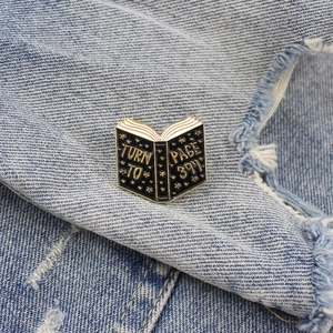 Creative black book enamel brooch with gold 'Turn to page 394' text on denim fabric
