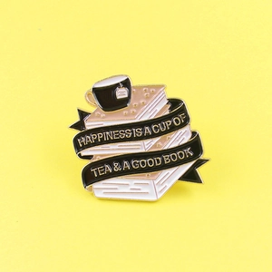 Enamel brooch featuring books and tea cup with ribbon slogan on bright background
