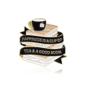 Enamel brooch with stacked books, black tea cup and golden motivational text on ribbon