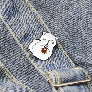 Cartoon white cat enamel pin badge drinking lemon tea on blue denim background