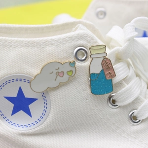 Cute enamel cloud and glitter drink bottle pins displayed on a canvas sneaker