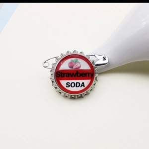 Close-up of a strawberry soda bottle cap brooch with red stripes and metal pin back