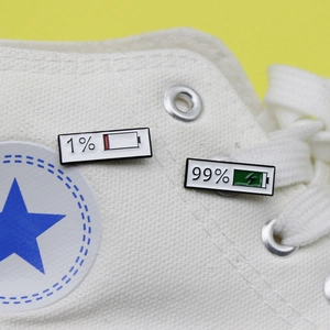 Creative battery status enamel pins with 1% and 99% charge designs on white canvas shoes