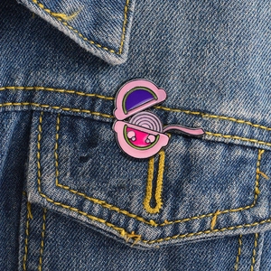 Close-up of a pink onion enamel pin with a cute face on a blue denim jacket pocket