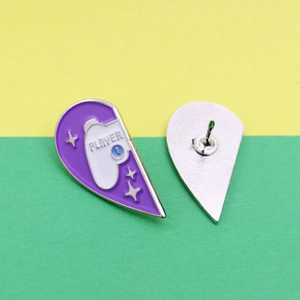 Detail view of purple heart-shaped enamel pin with Player 1 game controller design