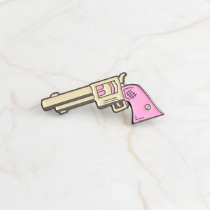 Macro shot of a cartoon enamel pin shaped like a cream and pink revolver on marble