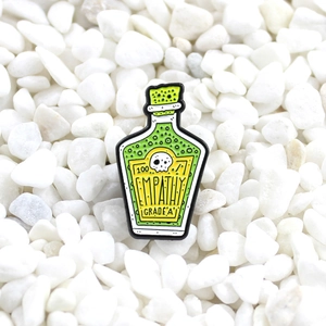 Creative green potion enamel pin with 100 Empathy Grade A text on white pebbles
