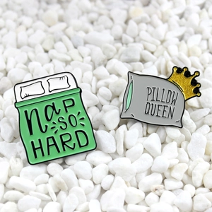 Detail of enamel pins featuring Nap So Hard green quilt and Pillow Queen crown designs