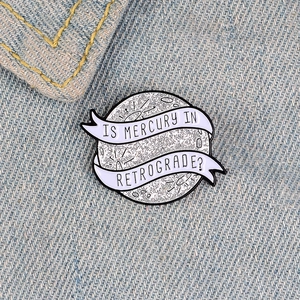 Close-up of a glittering planet enamel pin on blue denim fabric with creative text
