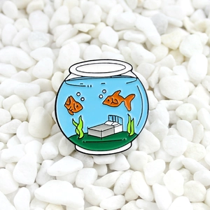 Creative fishbowl enamel pin with goldfish and bed on white pebbles background