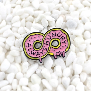 Pink infinity donut enamel pin with Always Hungry text on a white stone background