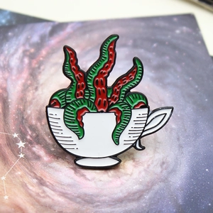 Close-up of enamel pin featuring a white coffee cup with red and green tentacles