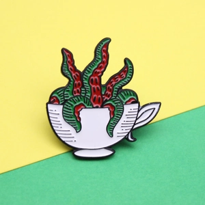 Creative enamel pin featuring a white teacup with surreal red and green tentacles