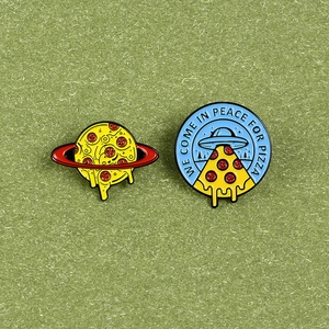 Creative spaceship and planet pizza enamel pins on green textured background