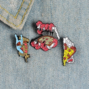 Close-up of three horror-themed pizza enamel pins featuring zombie hands and skull motifs