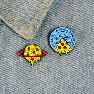 Close-up of creative pizza enamel pins on denim, showing spaceship and planet designs