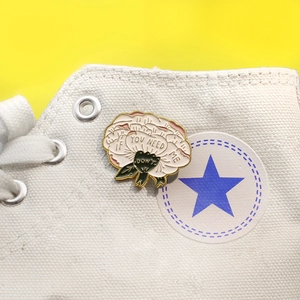 Close-up of pink flower enamel pin with gold edges on white canvas sneakers detail