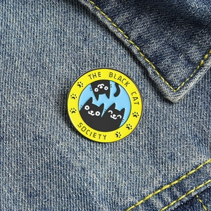 Épinglette émaillée de chat noir The Black Cat Society sur du tissu en jean bleu