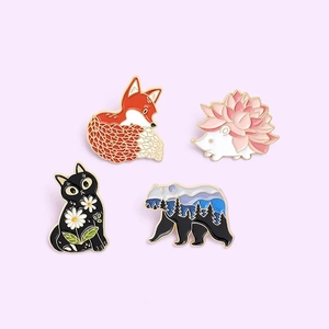 Close-up of animal enamel pins featuring fox, hedgehog, cat and bear on purple backdrop