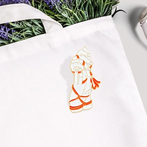 Artistic enamel brooch with hands holding a red ribbon, pinned on white canvas bag