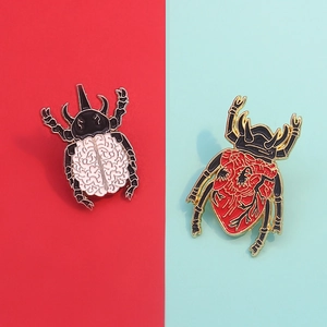 Creative enamel pins featuring heart and brain anatomy beetle designs on a split background