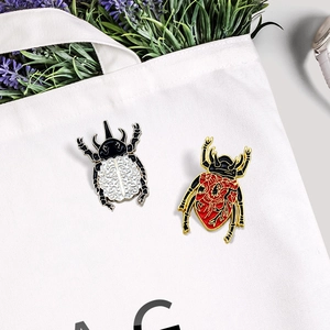 Artistic enamel beetle brooches with heart and brain patterns on a white canvas bag