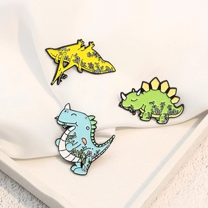 Détail de broches dinosaures colorées en émail aux motifs floraux sur tissu blanc