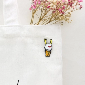 Cartoon white doll brooch with yellow antlers and S-logo pinned on a white canvas bag
