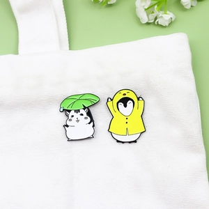 Cute enamel pins featuring a hamster with leaf umbrella and penguin in yellow raincoat